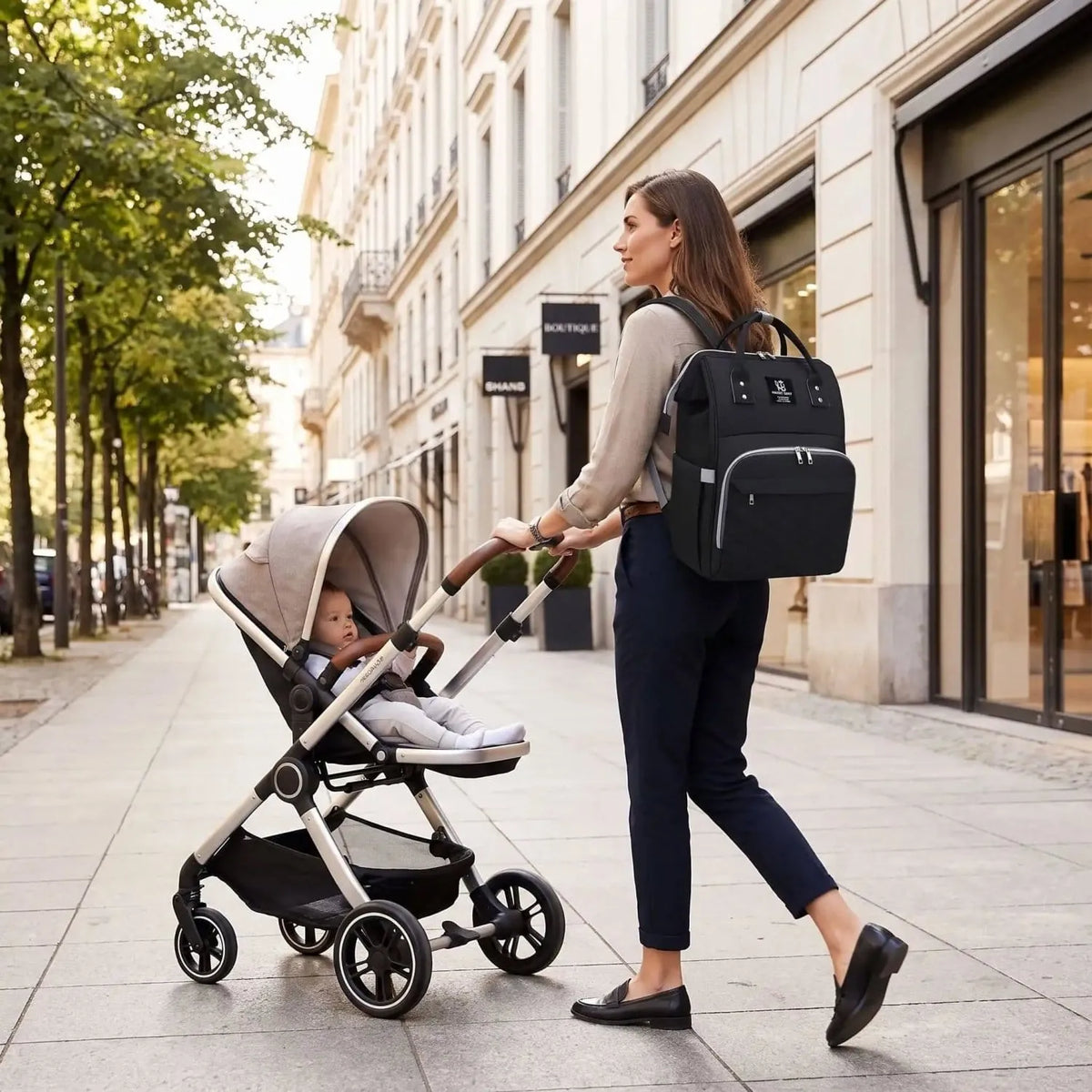 Sac à dos à langer Langeria noir porté par une maman qui pousse une poussette avec son bébé dans une scène urbaine naturelle